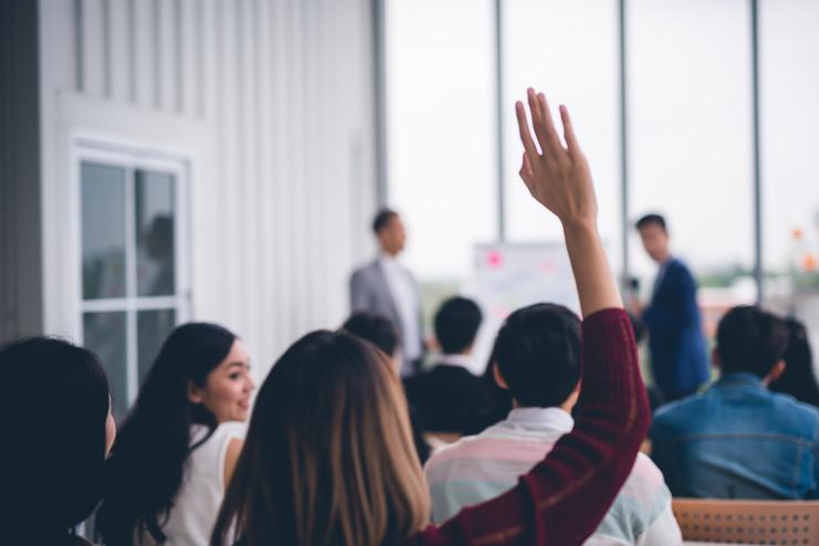 Abteilungsversammlung Bild zeigt eine Versammlung von Menschen in der eine Person sich meldet.