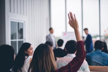 Abteilungsversammlung Bild zeigt eine Versammlung von Menschen in der eine Person sich meldet.